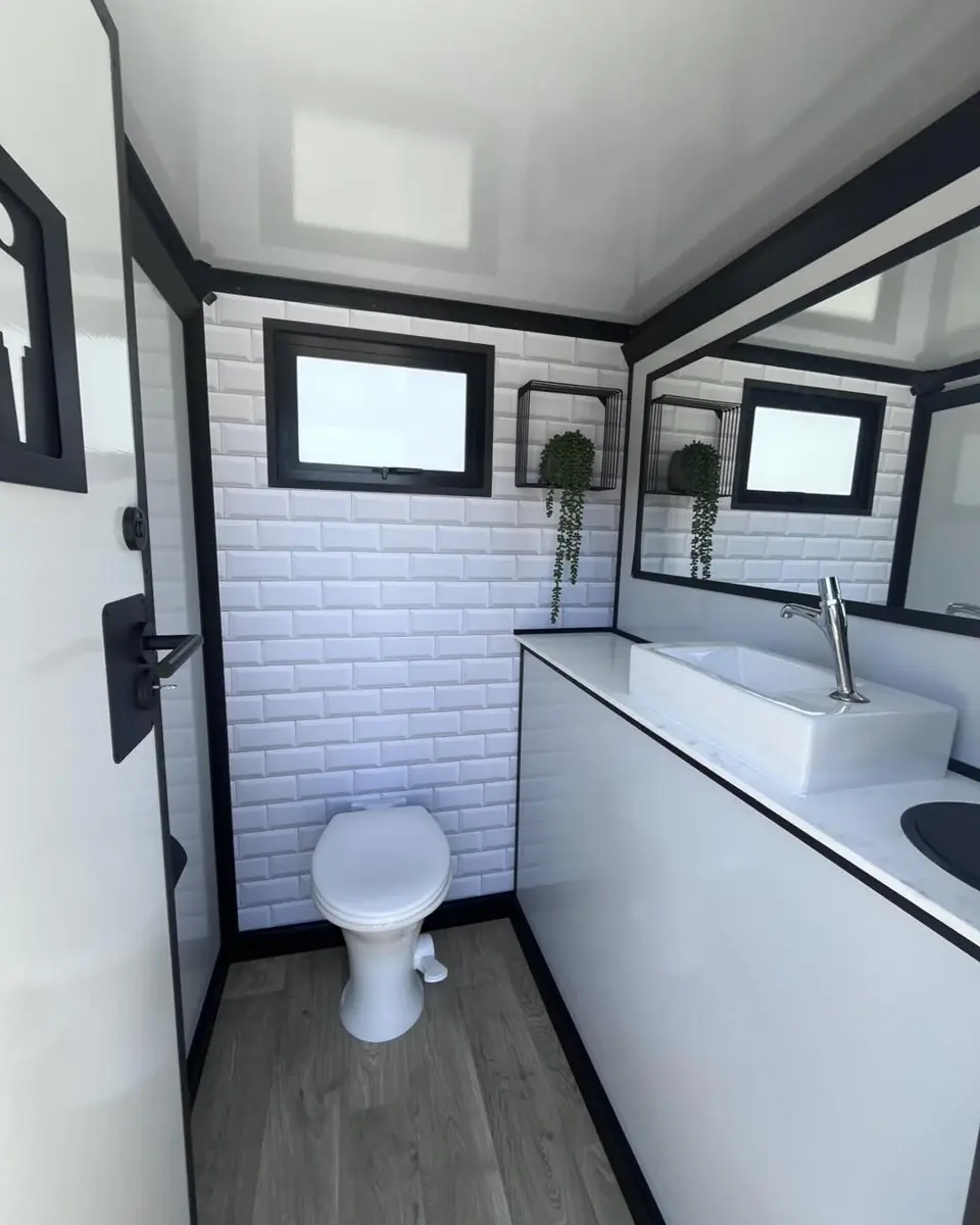 Inside a restroom trailer stall with tile wall, vanity and flushing toilet